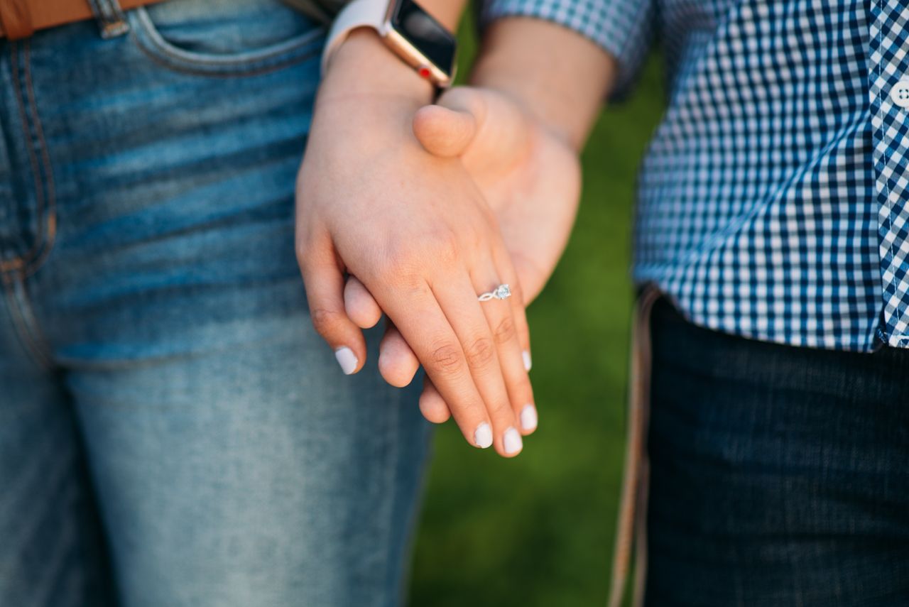 A man holds his fiancee’s hand out to show off her engagement ring and painted nails