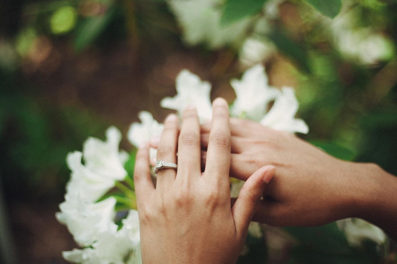 A woman with an engagement ring crosses her hands and rests them on a bouquet of white flowers