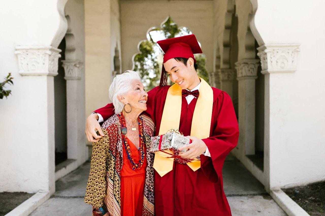 A college graduate and his grandmother smile at each other as they leave the university