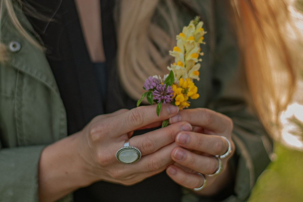 A close-up of a woman’s hands, wearing multiple rings, holding colorful spring flowers.