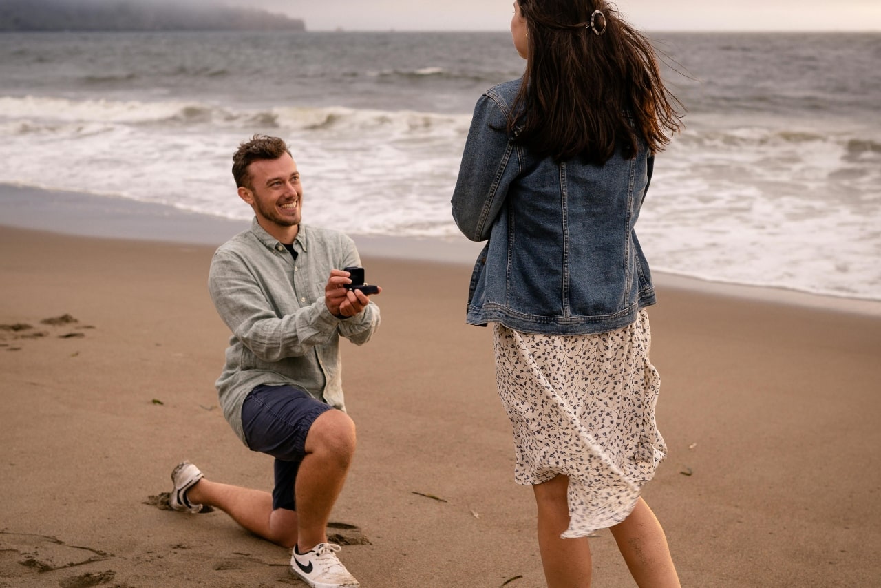 A view of a young man proposing to his happy partner on the beach.