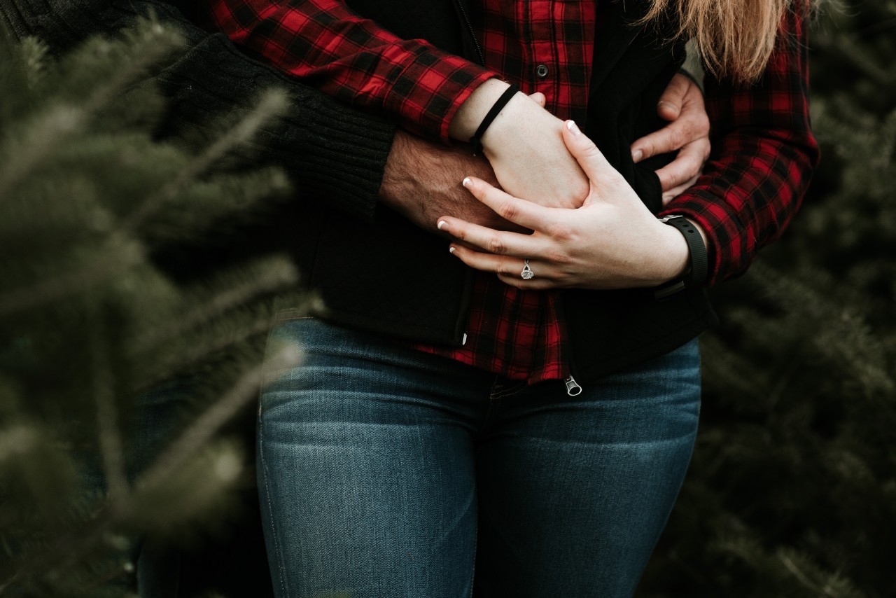 A bride-to-be being embraced from behind in a wooded area.