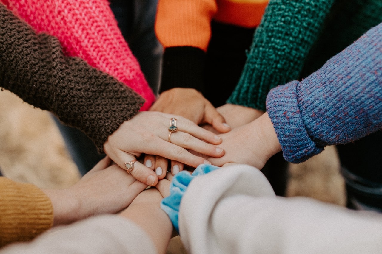 A close-up of hands placed in a circle, with emphasis on one person’s three rings.