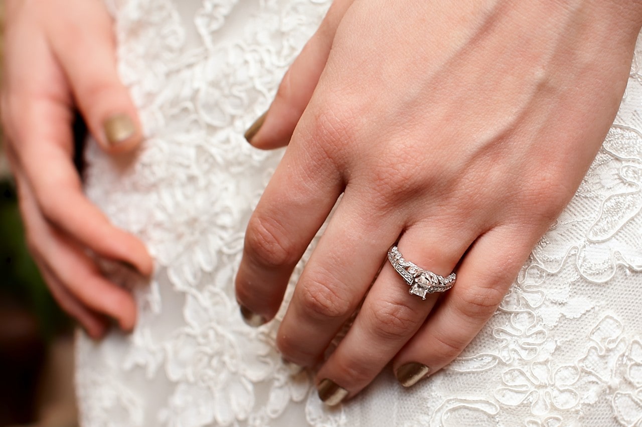 A close-up of a bride’s hands on her wedding dress, with emphasis on her stunning engagement ring.