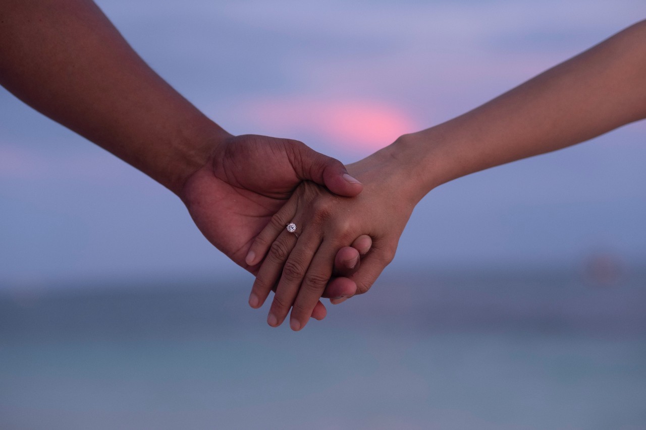 A couple holding hands, a beautiful dusk sky in the background.