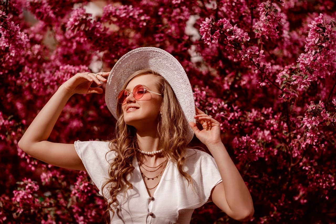 A stylish young woman posing in front of vibrant pink flowers.