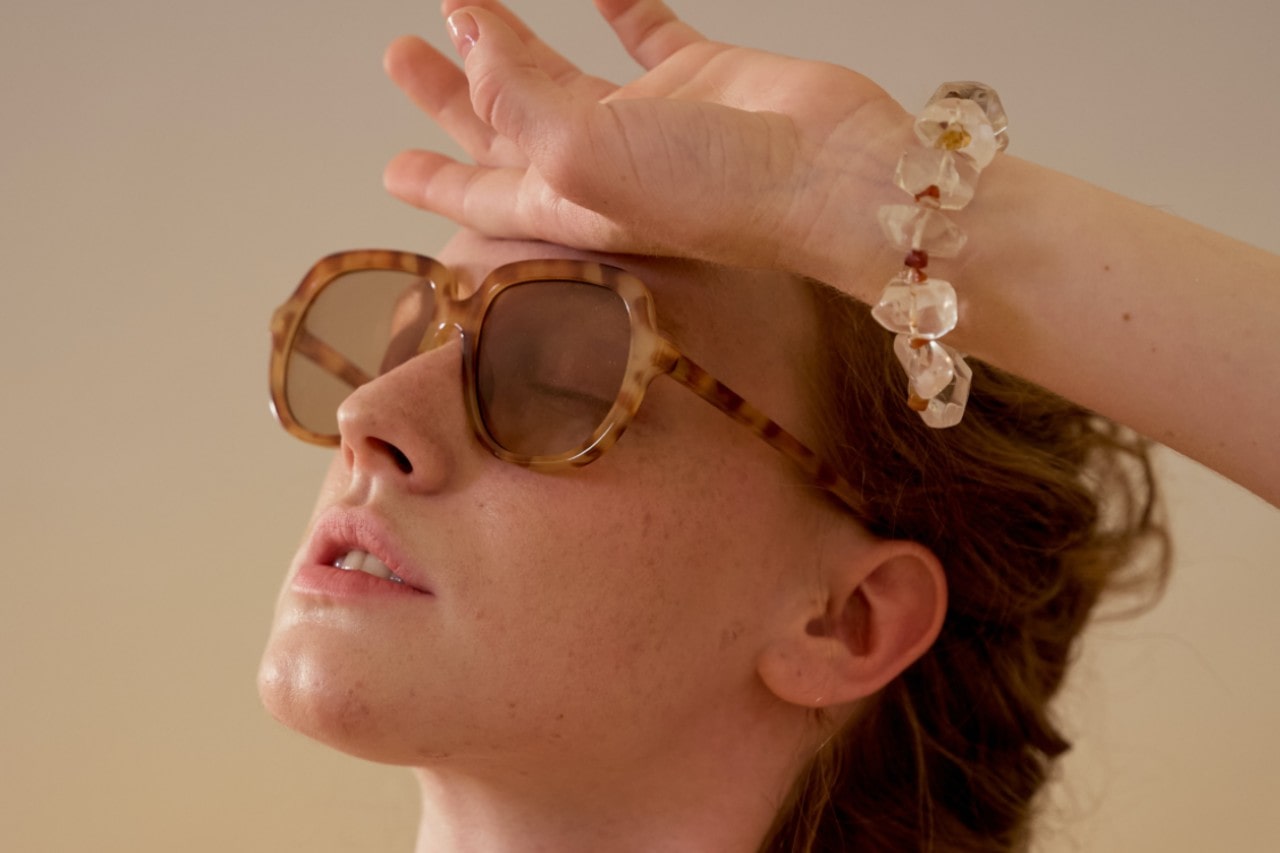 A woman poses wearing tortoiseshell sunglasses and a chunky bracelet.
