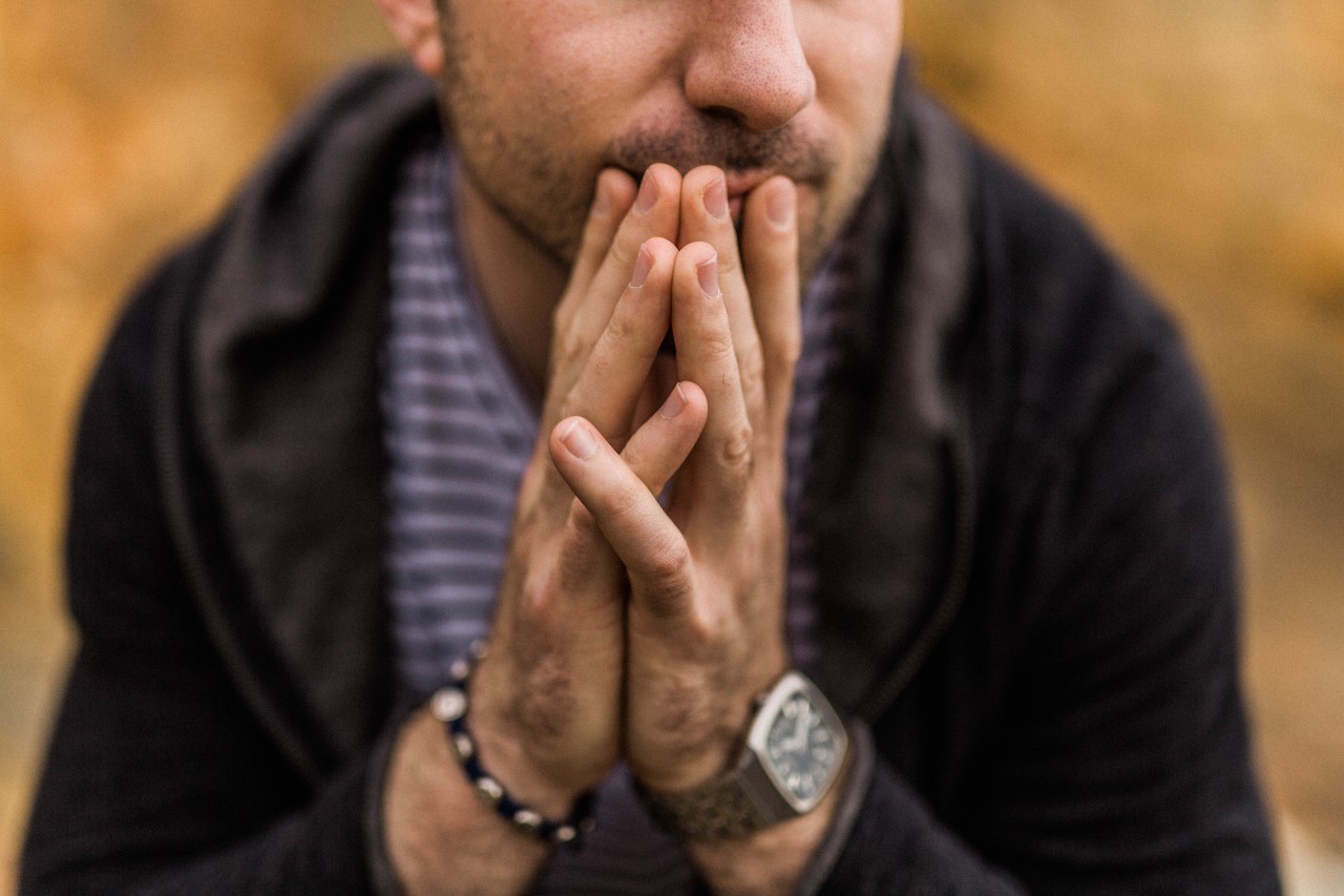 A man resting his hands on his mouth, his wrists adorned with jewelry.