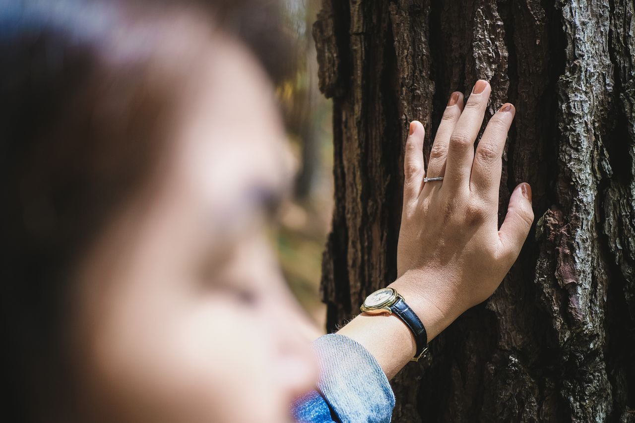 an engaged woman rests her hand on a tree during a hike.