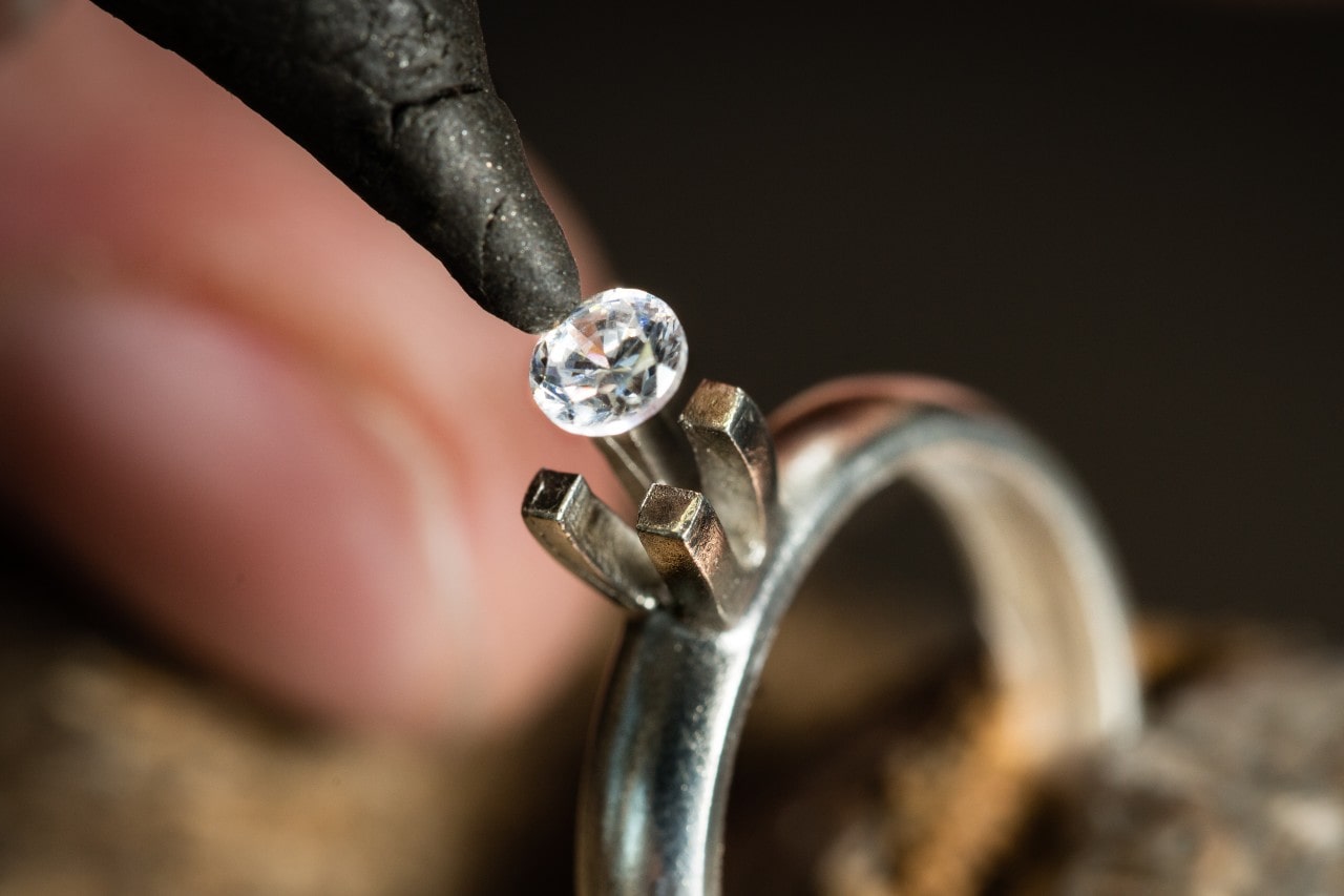 a jeweler inserts a round-cut diamond into a solitaire engagement ring setting.