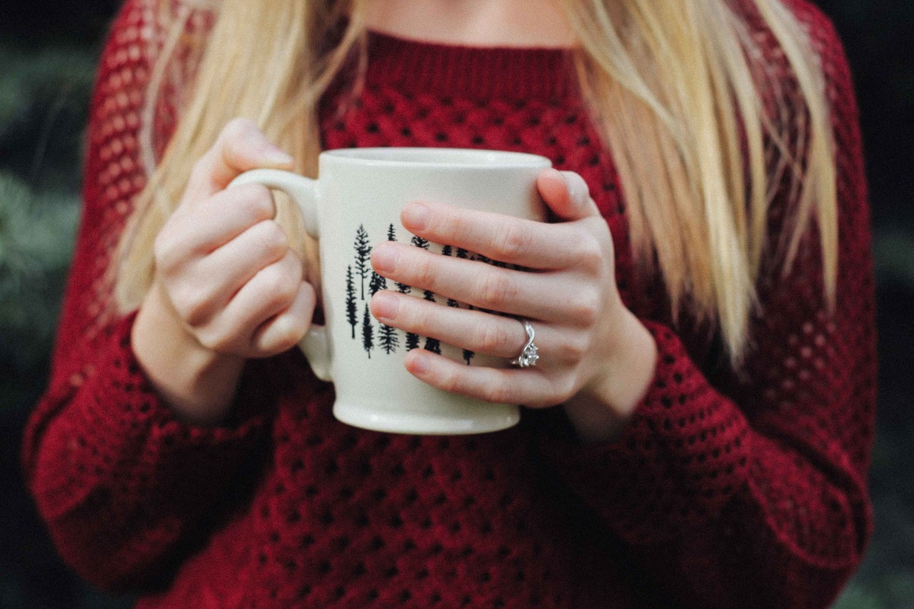 A woman in a sweater wears a platinum modern ring while sipping coffee.