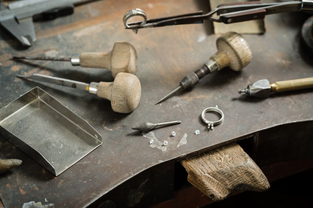 A jeweler’s desk features tools, rings, and diamonds scattered across it.