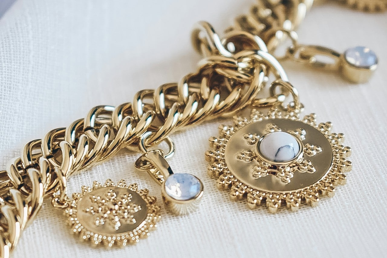 A close-up of a gold chain bracelet with intricate sunburst charms and white gemstones.