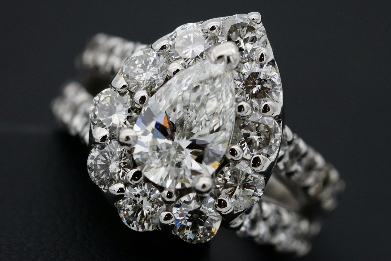 A close-up of an ornate split shank halo ring with a pear cut center stone. A close-up of an ornate split shank halo ring with a pear cut center stone.