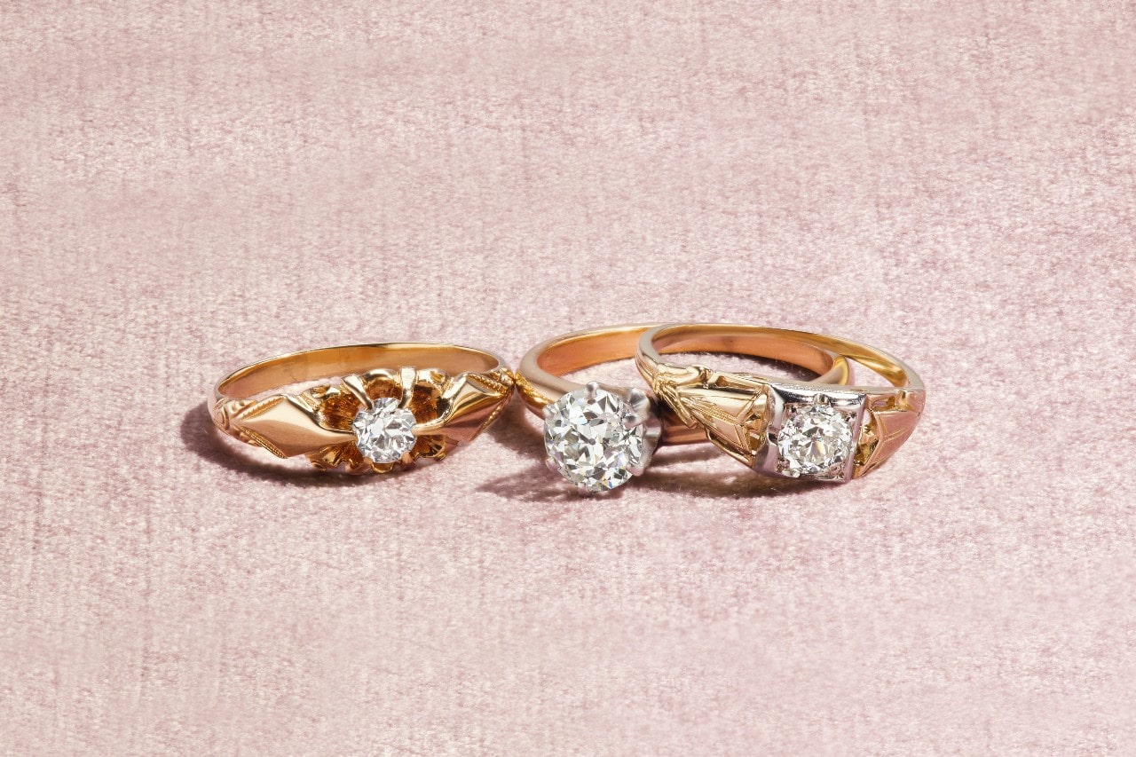 A close-up of three distinctive yellow gold solitaire rings, each featuring different details along the band. A close-up of three distinctive yellow gold solitaire rings, each featuring different details along the band.