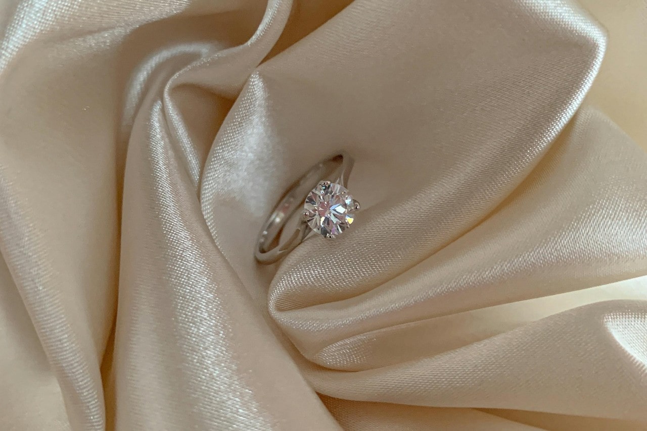 A close-up of a simple yet elegant engagement ring nestled in beige fabric. A close-up of a simple yet elegant engagement ring nestled in beige fabric.