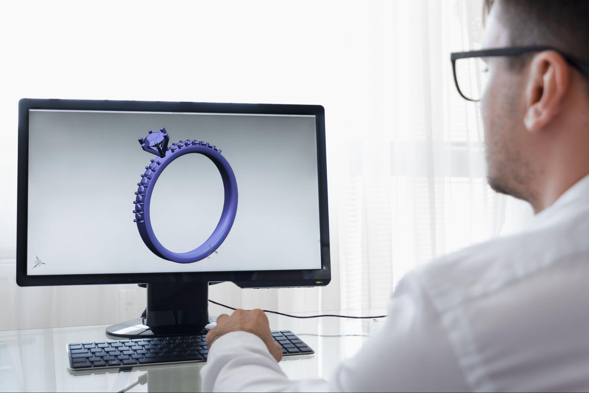 A man views a 3D digital model of a diamond engagement ring on a computer screen, using software for jewelry design.