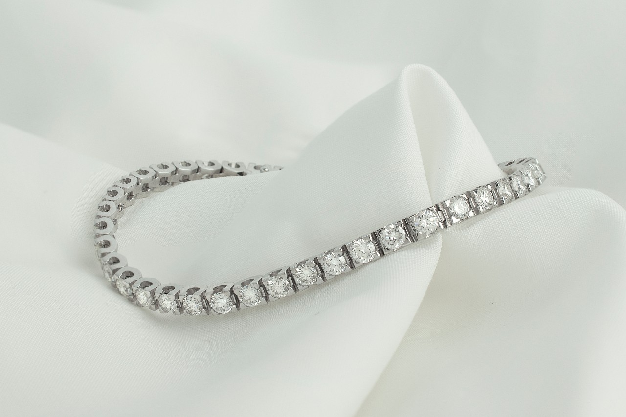 A white gold and round diamond tennis bracelet on a white fabric