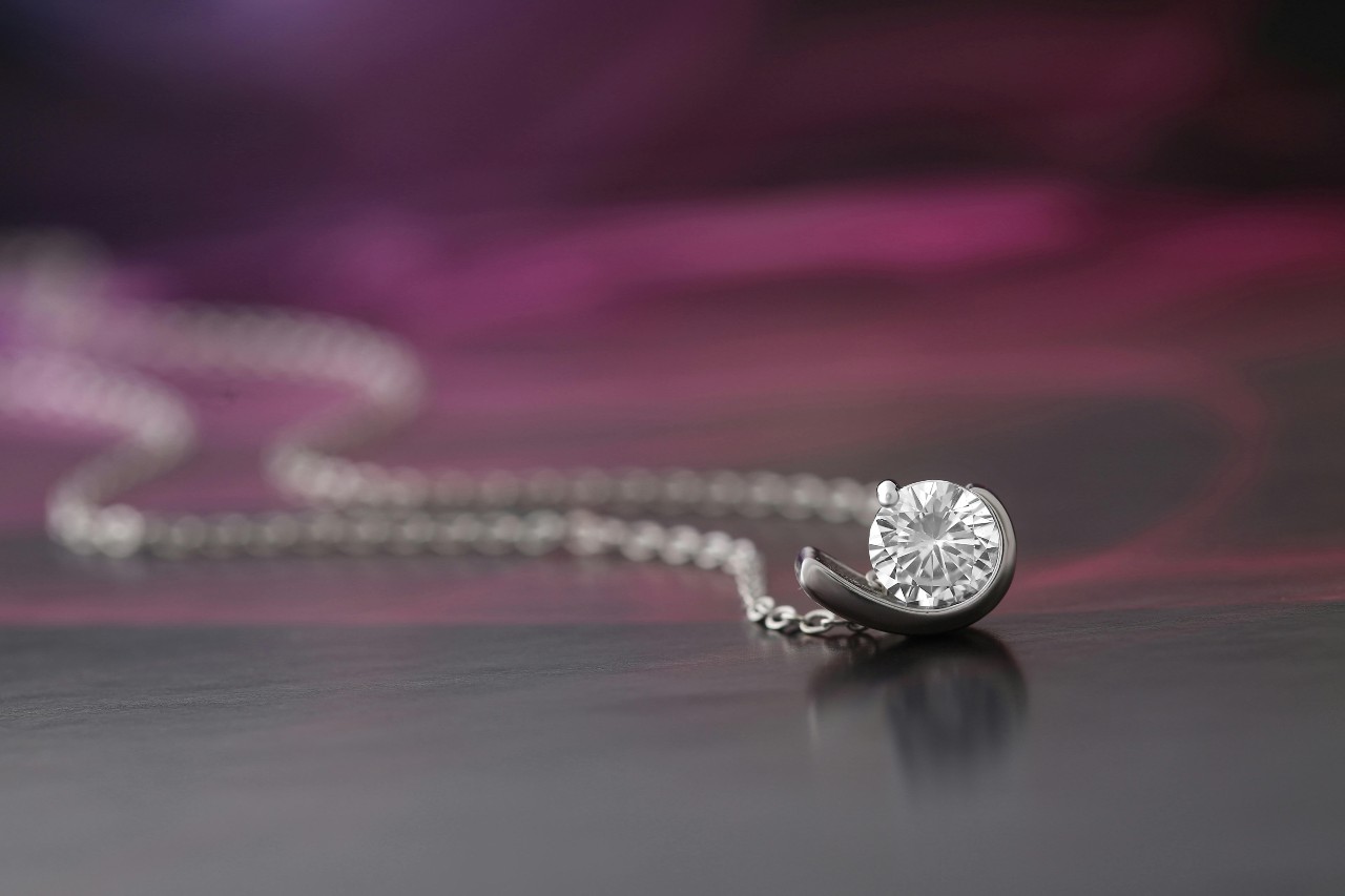 A close-up of a simple yet elegant diamond pendant necklace on a dark background.