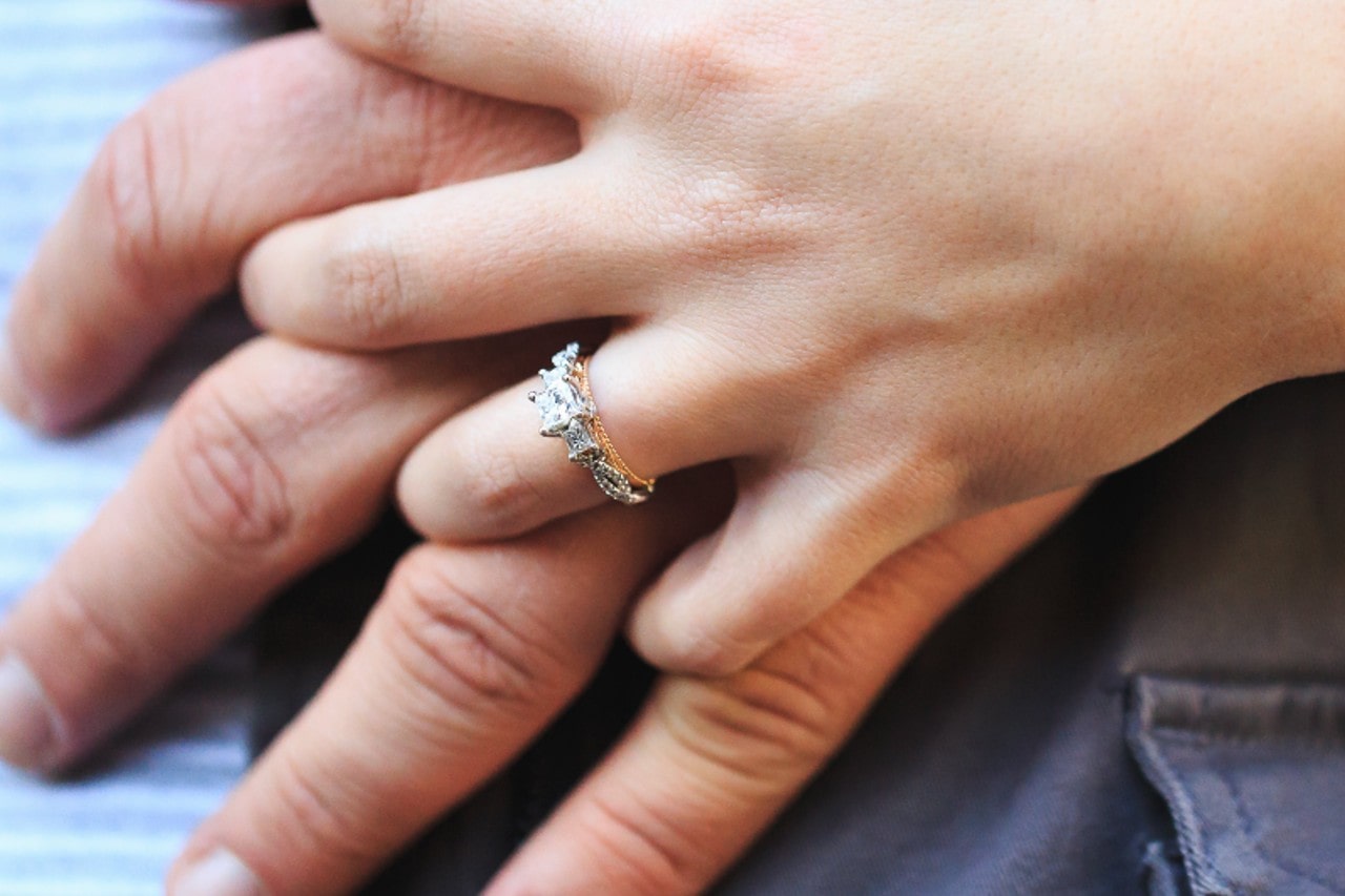 a woman holding a man’s hand, wearing a mixed metal, three stone engagement ring