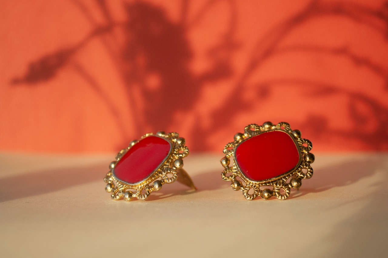 A pair of yellow gold earrings with large red gemstones on a beige surface.