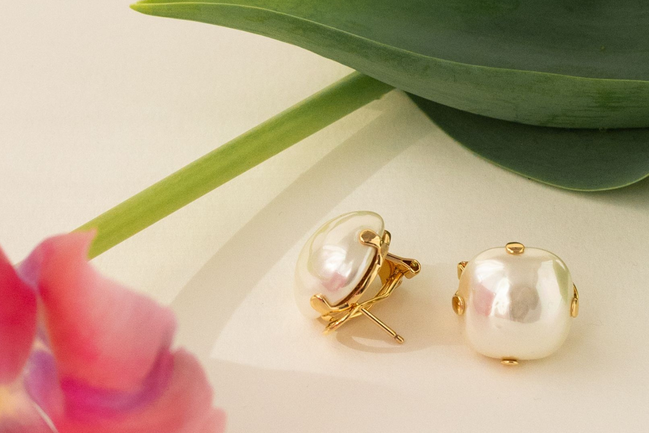 Pearl stud earrings in yellow gold placed on a beige surface near the tulip. Pearl stud earrings in yellow gold placed on a beige surface near the tulip.