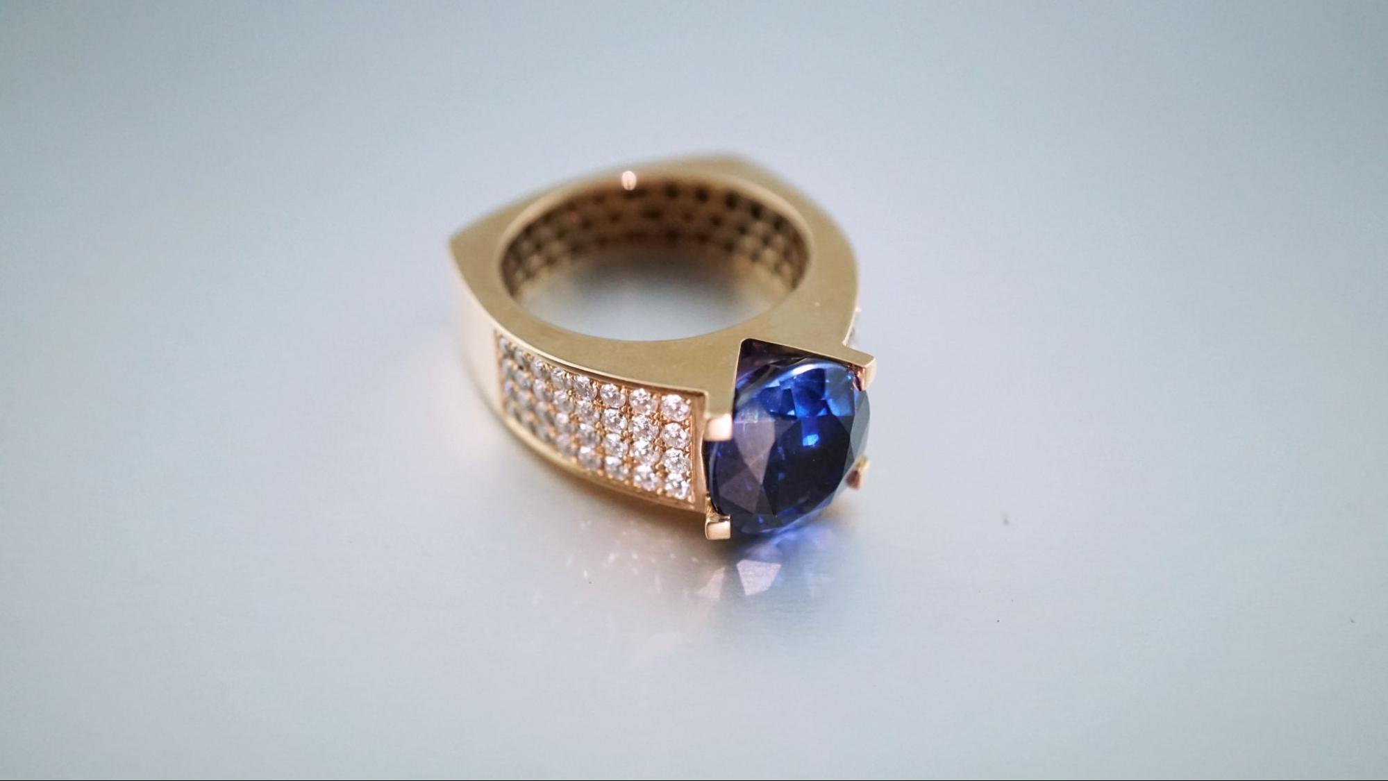 A yellow gold fashion ring with several rows of diamonds and sapphire as a centerpiece. A yellow gold fashion ring with several rows of diamonds and sapphire as a centerpiece.