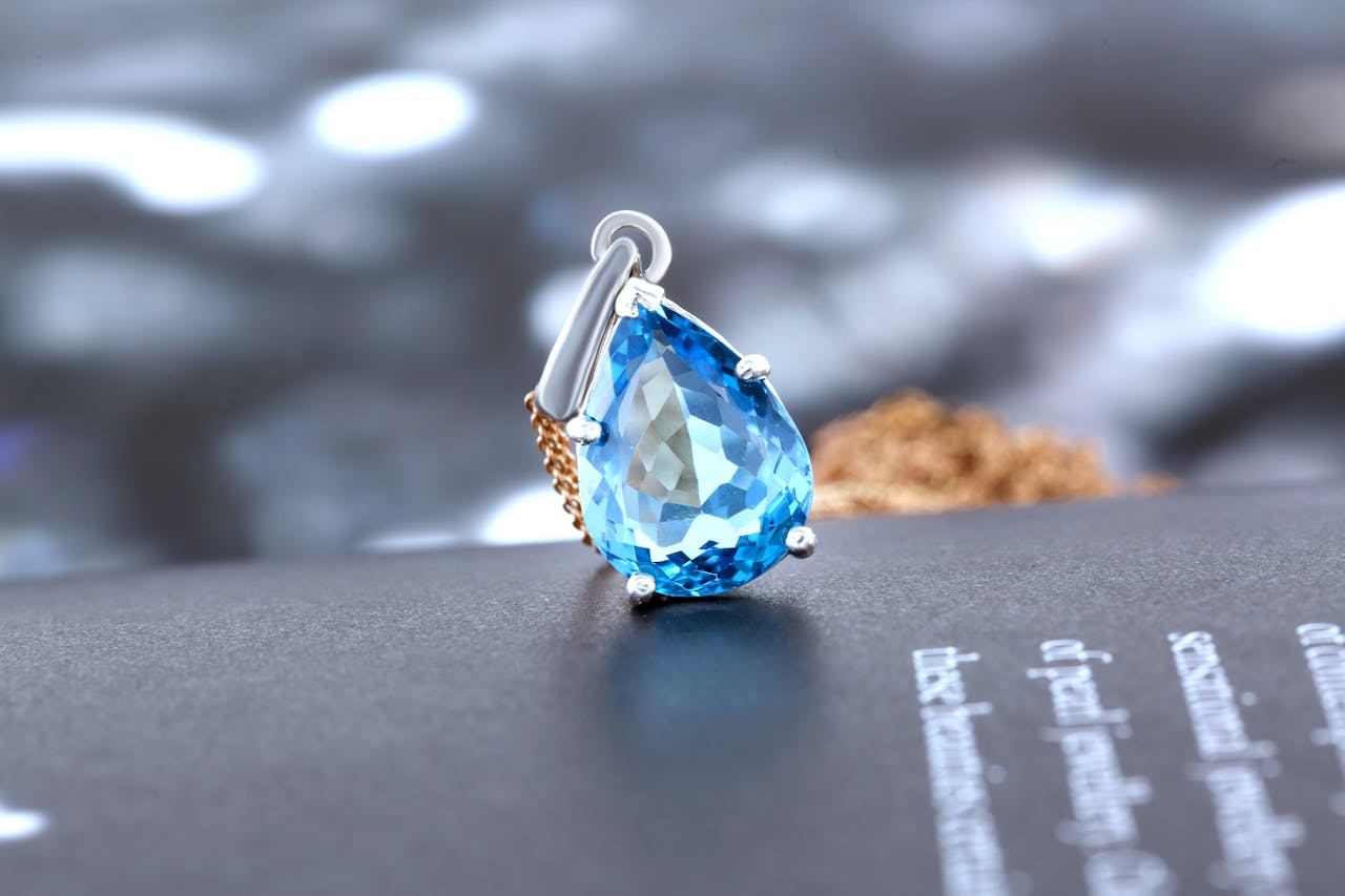 A close up of a pear shaped sapphire pendant on top of the black magazine page. A close up of a pear shaped sapphire pendant on top of the black magazine page.