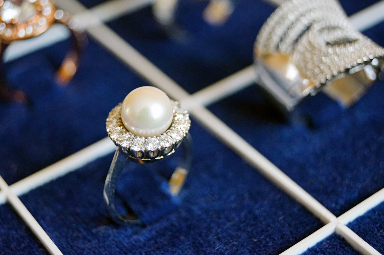 A close-up of dazzling fashion rings, with emphasis on a halo ring with a pearl center stone. 