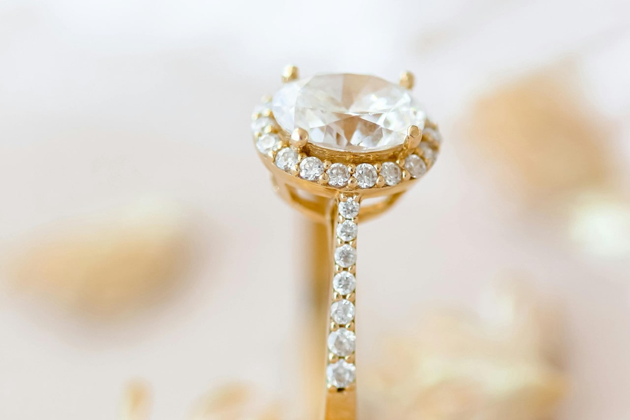 A close-up of a stunning gold engagement ring, with side stones and a halo setting.