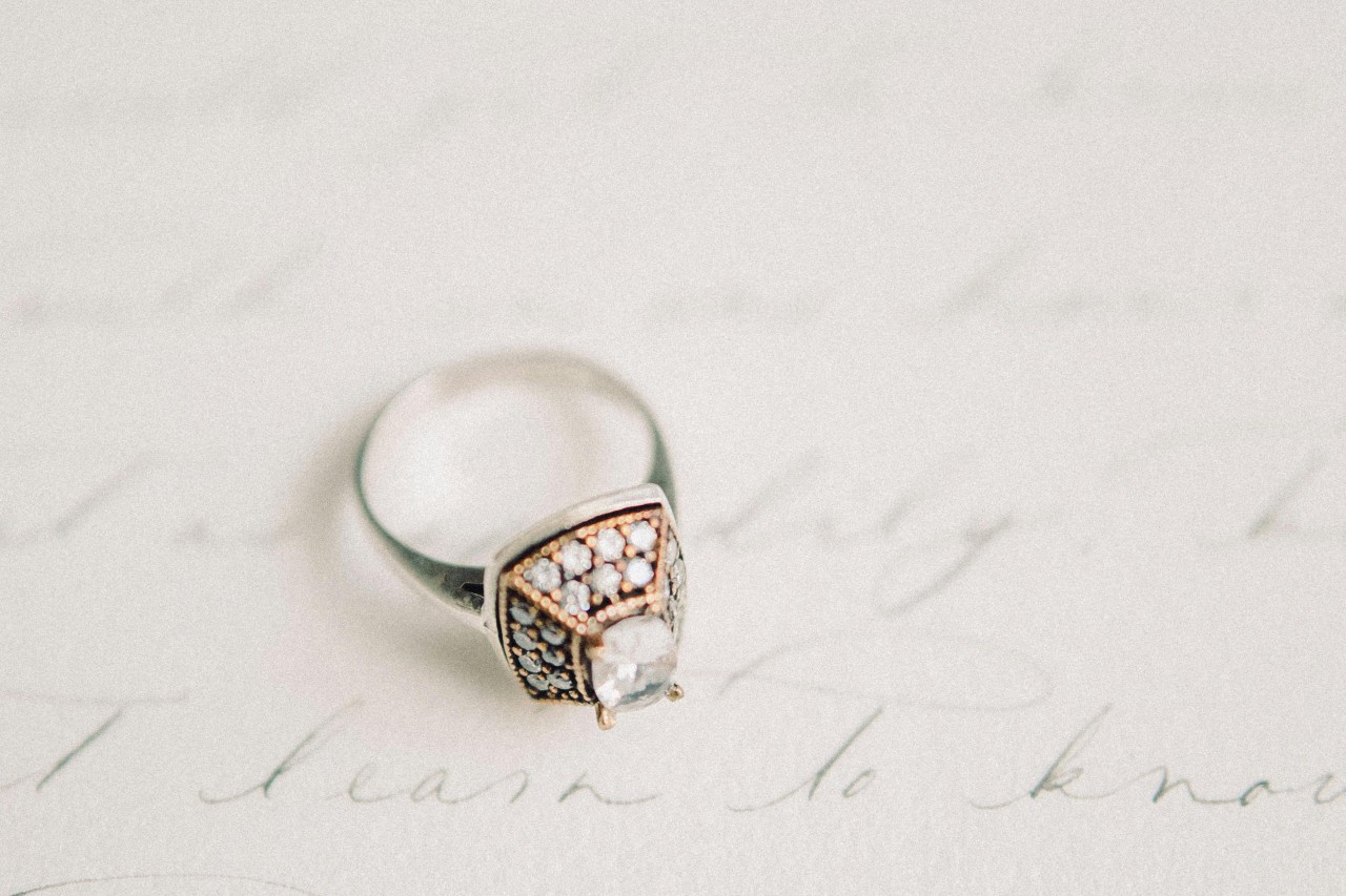 A unique and ornate engagement ring displayed atop hand-written wedding vows.