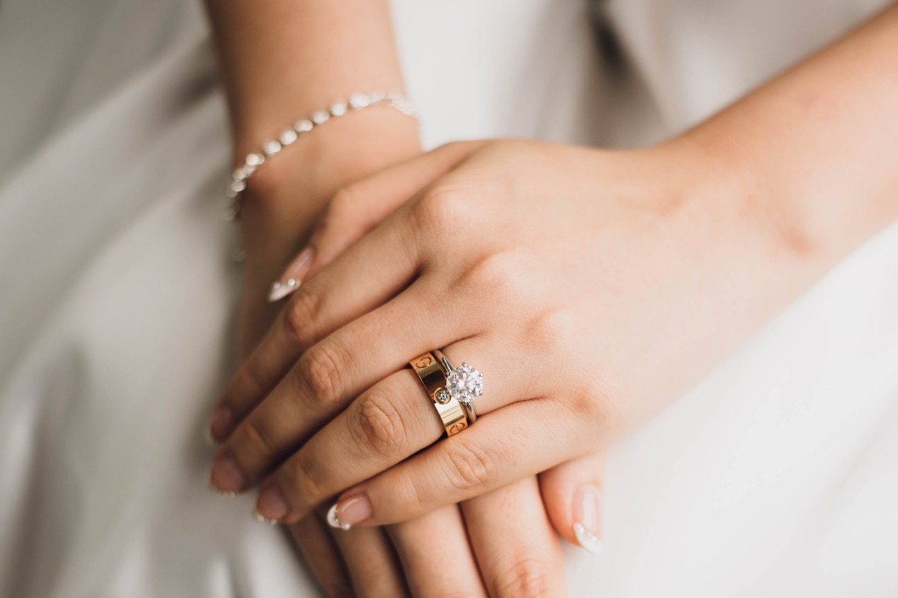 A close-up of a bride’s hands, adorned with a yellow gold wedding band and solitaire diamond engagement ring. A close-up of a bride’s hands, adorned with a yellow gold wedding band and solitaire diamond engagement ring.